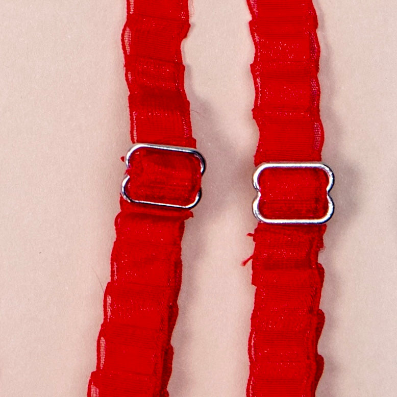 Close up on a set of interchangeable her-rah bra straps in a pleated organza patterns with a sheer shimmer to the fabric in color Cherry Tart (red).