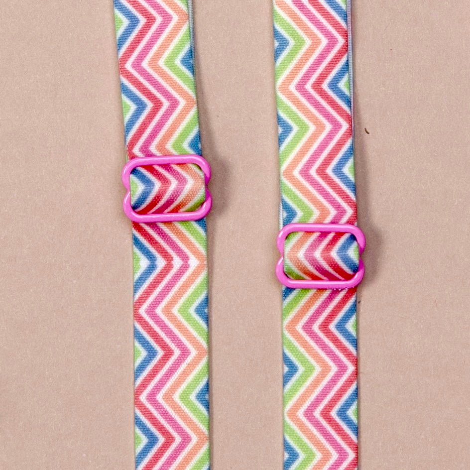 Close up on a set of interchangeable her-rah bra straps in chevron patterns with alternating stripes of pastel rainbow colors (including: blue, green, orange, pink, red, and white).